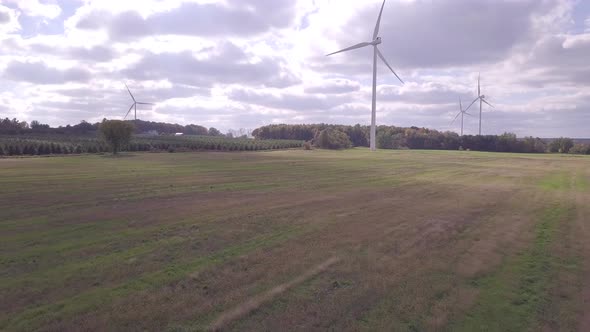 Flying low over field and farmland.  Camera moves towards wind turbine with other windmills in backg alt