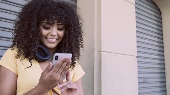 Beautiful woman with afro curly hair with cell phone and headphones