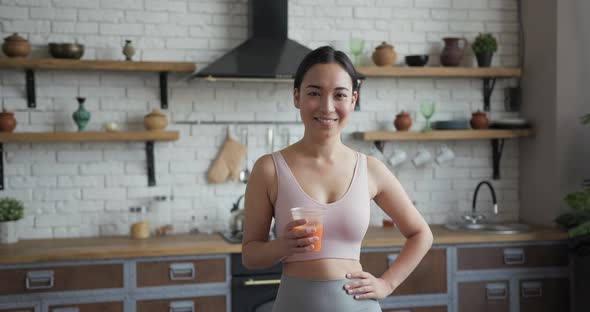 Healthy Asian Woman Standing in the Kitchen with Orange Fresh Juice in Her Hands alt