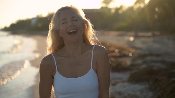 Slow motion of mature woman backlit on beach swinging her hair and playing with it with hands then s alt