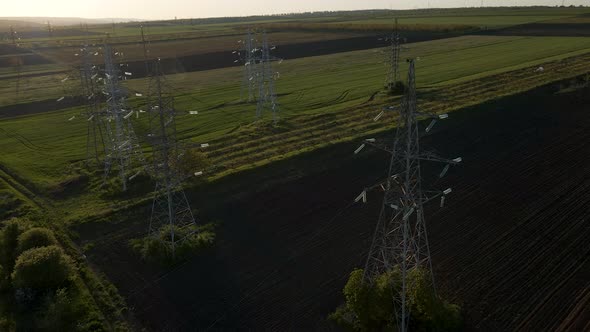 Drone Flying Over Transmission Tower Supporting an Overhead High Voltage Power Line at Sunset alt