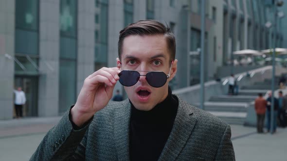 Shocked Young Businessman Takes Off His Sunglasses in Surprise. Astonished Man Scared By the News alt