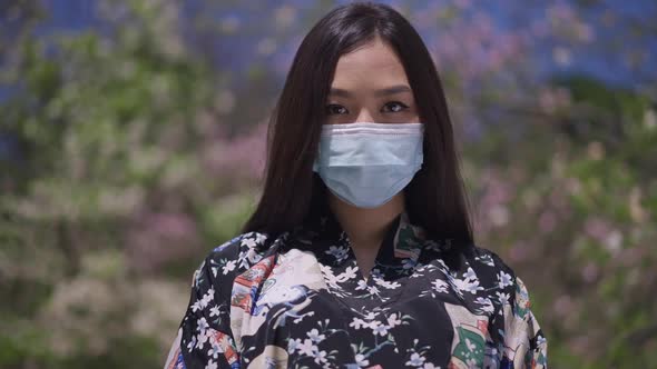 Live Camera Zoom in to Serious Asian Young Woman in Kimono and Coronavirus Face Mask Looking at alt