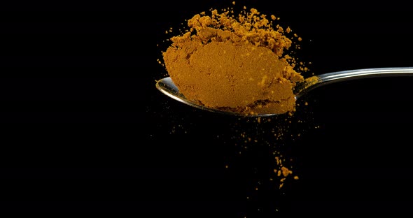 Spoon and Curry Powder falling against Black Background, Slow motion 4K alt
