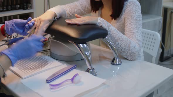 Unrecognizable Person in Gloves Saws Nails of Young Woman in Salon alt