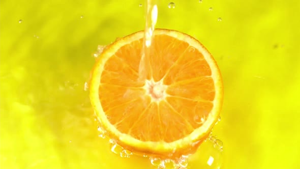 Water pours on an orange juicy orange on a yellow background slow motion closeup. Orange slice alt