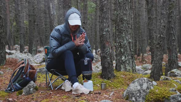Woman Hiker in Forest Camping Waits Cooking Tea in Gas Burner and Pours in Mug