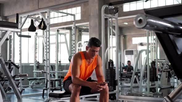 Athletic man relax sitting and texting message on smartphone at gym