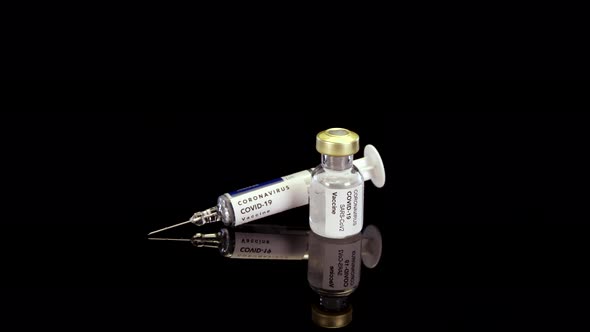 Coronavirus vaccine in ampoule and syringe rotating on a black background.  Mock up video