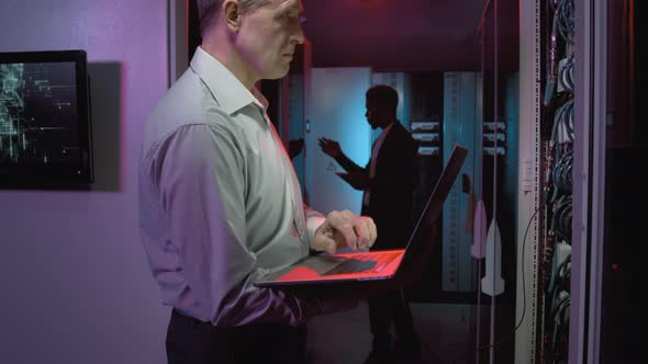 Middle-Aged Network Engineer Working on Laptop in Data Center alt