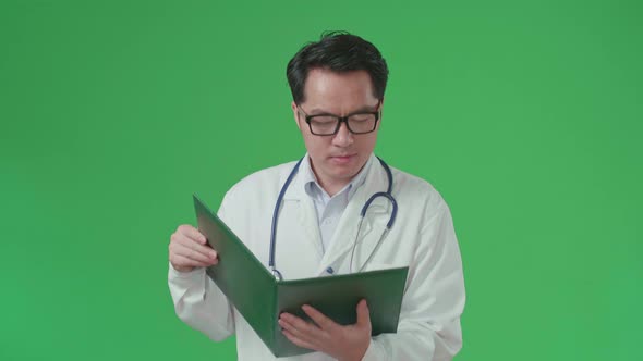 Asian Doctor With Stethoscope Reading Document While Walking On Green Screen Chroma Key alt