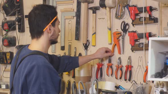 Young Carpenter in Uniform Selects a Suitable Tool for Wood Work alt