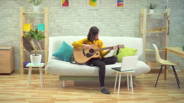 Young Woman Playing Guitar Learning on the Internet in Modern Apartments alt