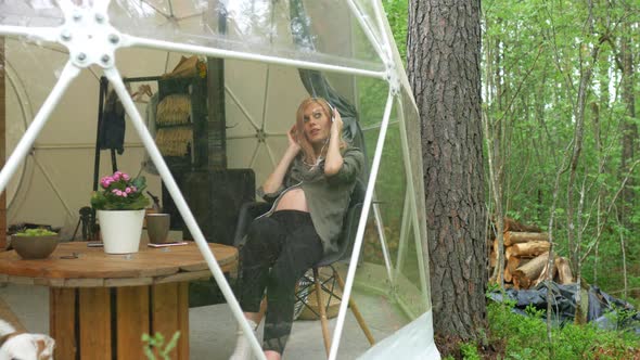 pregnant woman listens to music with headphones while sitting in a dome tent alt