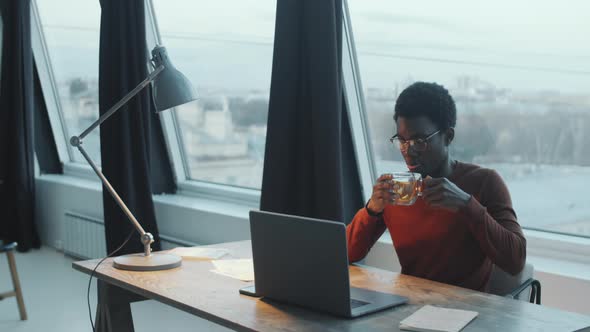 Black Man Using Laptop and Drinking Tea in Rooftop Office alt