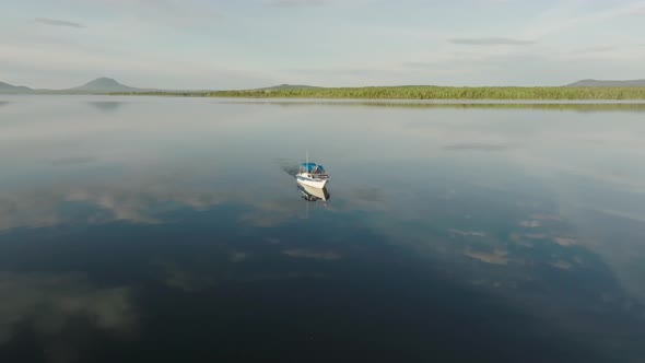 A boat alone crossing flat calm lake reflecting clouds alt