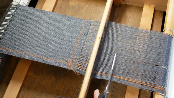 Hand with scissors cuts the warp threads off the wooden frame. Finishing the woven project