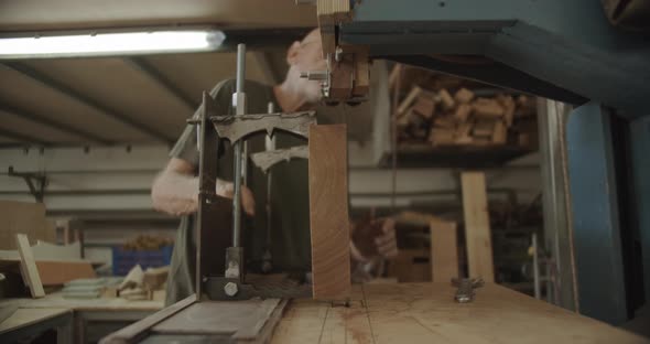 old Carpenter pulls a wooden block on a saw