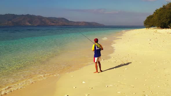 Man fishing alone on paradise bay beach vacation by blue sea with clean sandy background of Gili Men alt