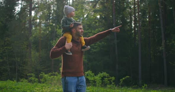 Slow Motion: Son Sitting on His Fathers Neck in the Spring Sunny Park. Fathers Day alt