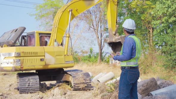 Construction worker controls digging of trench with  excavator on site.