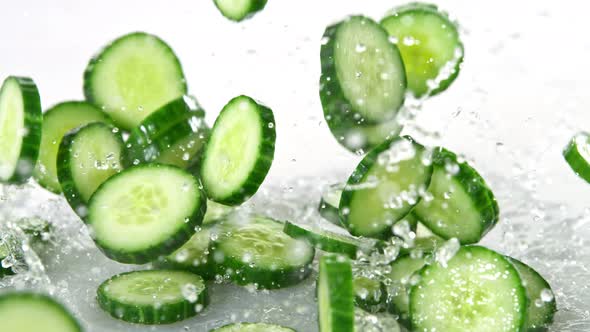 Super Slow Motion Shot of Cucumber Slices Falling Into Water on White Background at 1000Fps alt