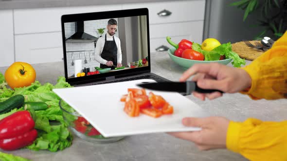 Housewife in Kitchen Knives Sliced Tomato From Cutting Board Into Salad Bowl alt