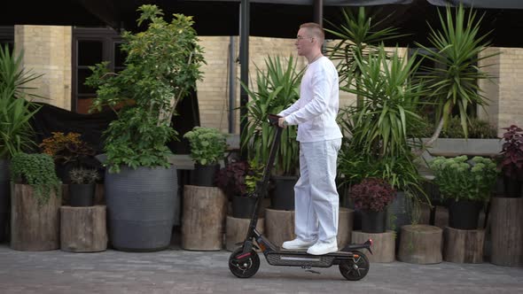 Side View Young Man Riding Escooter on City Street on Spring Summer Day alt