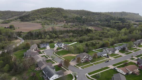 Drone view of rural midwest valley neighborhood in summer with farmland, forest and bluffs.