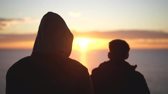 Two Male Friends Standing at Sea Shore or Ocean Coast Watching Sunset Together