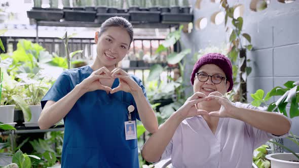 nurse and an elderly woman suffering from cancer make a heart-shaped hand in a nursing home