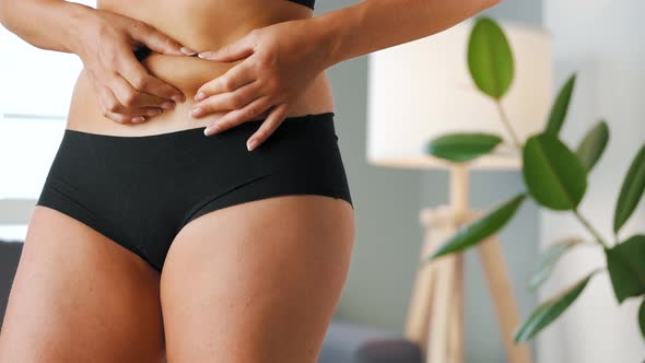 Woman Compressing the Skin on Her Stomach Checking for Cellulite and Excess Subcutaneous Fat alt