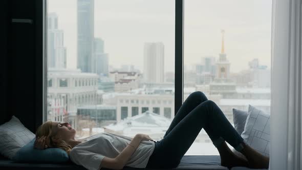 woman sleeping by a large window overlooking the city