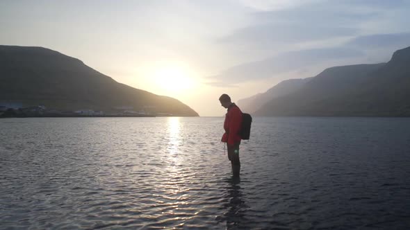 Man Looking Down Into Shallow Waters At Sunrise alt