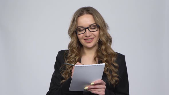 Woman in a Business Suit Writes in a Notebook Then Nervously Tearing Out a Page on a Gray Background alt