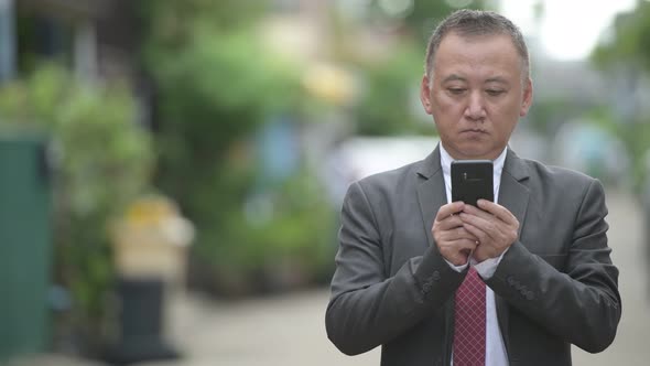 Mature Japanese Businessman Using Phone in the Streets Outdoors alt