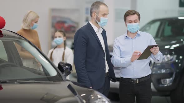 Young Dealer Consulting Client in Car Dealership on Coronavirus Pandemic alt