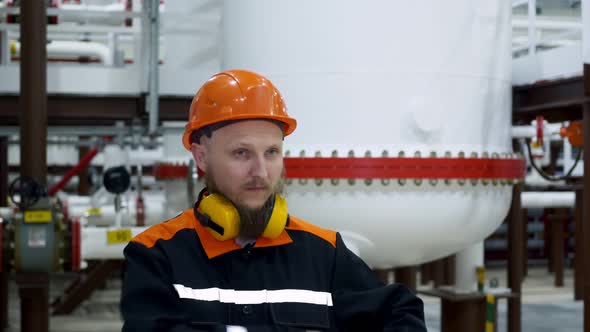 A Bearded Mechanic in a Working Helmet is in a Gas Compression Workshop Transmits Readings on a alt