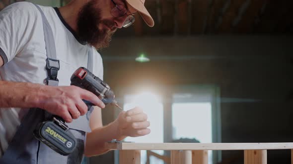 Male Builder Using Electrical Screwdriver to Connect Two Wooden Pieces in Studio