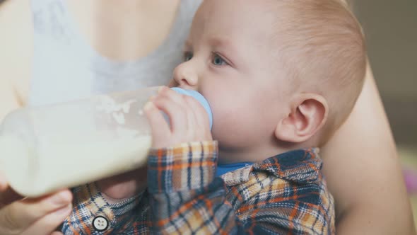 Lovely Boy Eats Food From Bottle in Mother Arms Closeup alt
