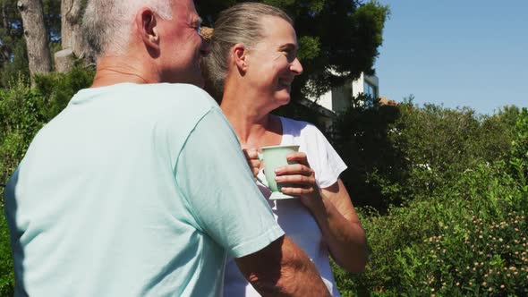 Caucasian senior couple holding coffee cup talking to each other in the balcony at home alt