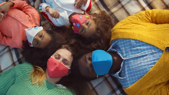 Top View of Happy Diverse Family in Safety Mask Relaxing on Blanket During Picnic alt