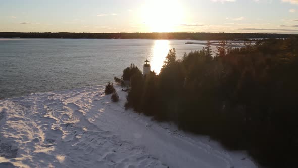 Old Presque Isle Lighthouse in Michigan during the winter with a sunset. alt