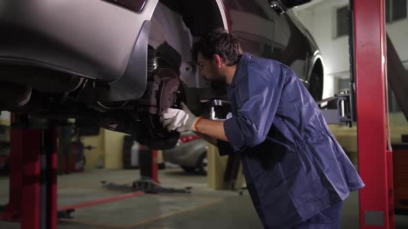 Repairman with Flashlight Checking Car Chassis alt