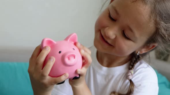 Smiling Child Girl is Shaking Piggy Bank