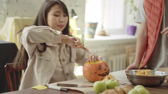 A Beautiful Young Lady is Taking the Pulp Out of the Pumpkin and a Young Man is Watching alt