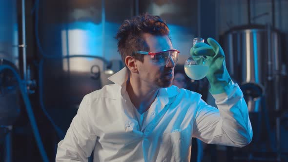 Mad Scientist Drinking Blue Liquid From Glass Flask in Industrial Lab alt