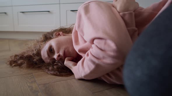 Zoom in video of depressed young caucasian woman lying in the floor. alt
