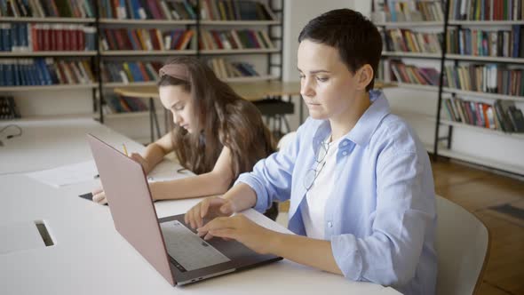 Woman Types on Laptop and Daughter Works at School Project