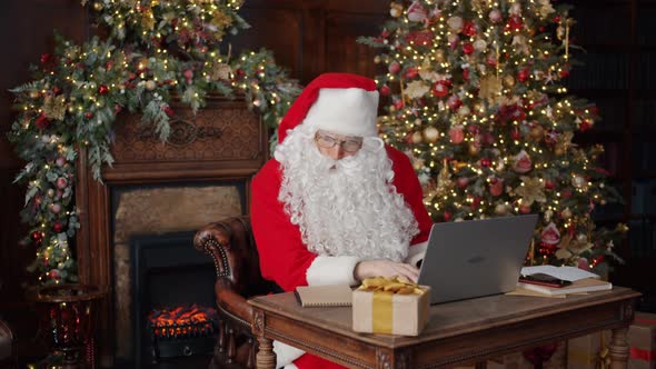 Santa Claus Using Laptop Typing Focused on Work in Decorated House on New Year Day alt